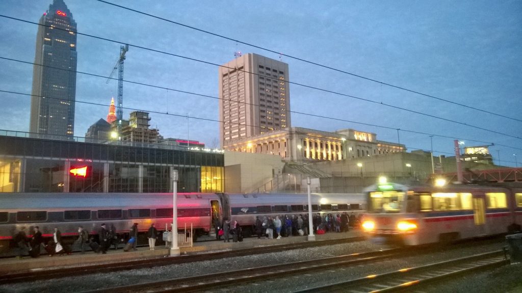 Lots of passengers getting on an Amtrak train at dawn in Cleveland, Ohio with an RTA train passing by.
